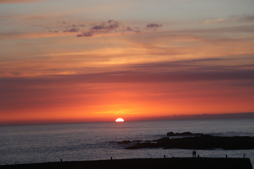Warm red glow of the sun just dropping down below the horizon at Sennen Cove, cornwall